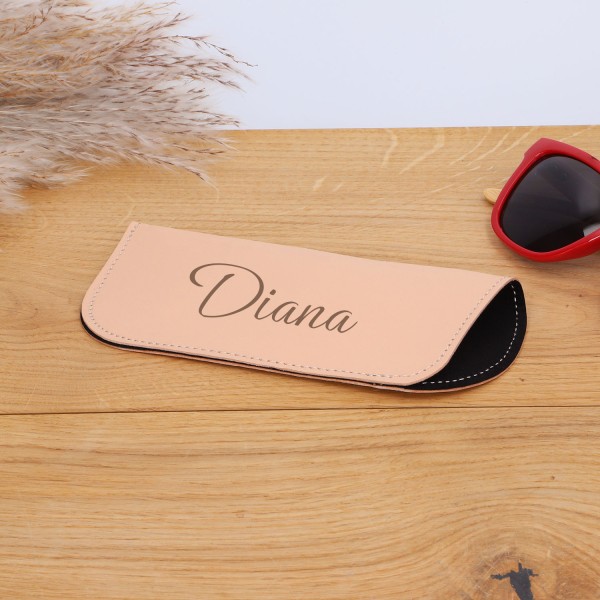 Brillenetui beige mit graviertem Namen auf Tisch liegend (Sonnenbrille teilweise sichtbar am Bildrand)