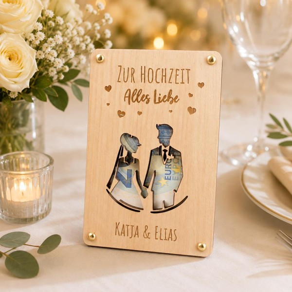 Geldgeschenk Verpackung Hochzeit (Holz, personalisiert mit Gravur) - im Hintergrund Brautstrauß und Sektglas (am Bildrand abgeschnitteen